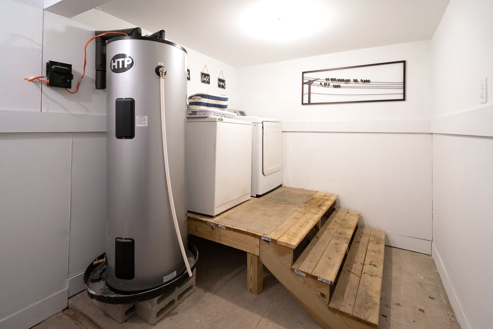 A compact bathroom with a built-in water heater, a small white washing machine, and a wooden bench.