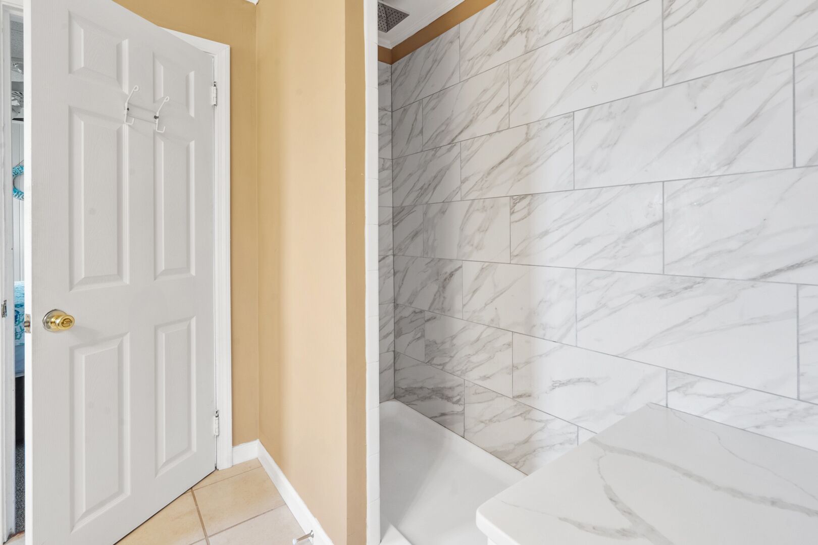 Une salle de bain avec une porte blanche, des murs de couleur beige et des carreaux de marbre.