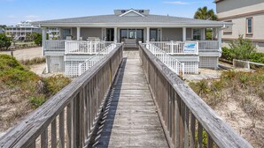 Ein Strandgrundstück mit einer Holzpromenade, die zu einem Haus mit überdachter Veranda und einem Schild für Thomas Immobilien führt.