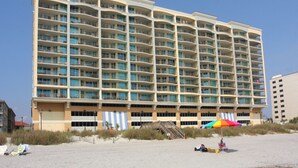 Un hôtel à plusieurs étages doté de balcons, situé en bord de mer et agrémenté d’un parasol coloré.