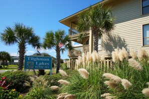 Señal que indica 'Tilghman Lakes by the Sea', con un edificio que tiene balcón y jardines tropicales.