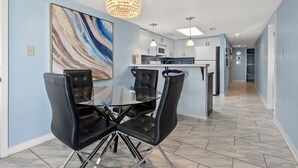 A modern kitchen with a central island, a dining area with black leather chairs, and a large abstract painting on the wall.