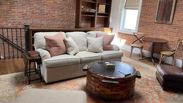 A cozy living room with a brick wall, a sofa, a coffee table, and a bookshelf.
