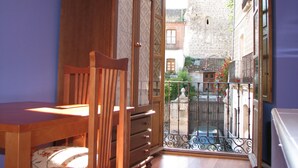 Une pièce comprenant une armoire en bois, une chaise en bois, une table et donnant sur une cour avec une porte et des bâtiments.