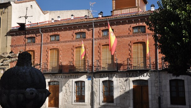 Un bâtiment doté de nombreux balcons, une statue au premier plan et des drapeaux suspendus à la façade.