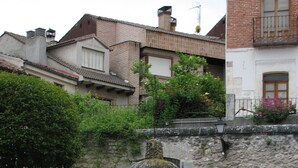 Une fontaine en pierre se trouve dans une cour, avec un mur en pierre et un bâtiment en arrière-plan.