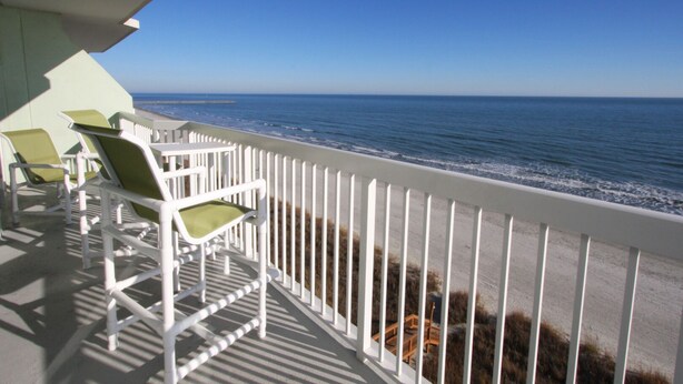 A balcony with white railings and green chairs overlooking the ocean.