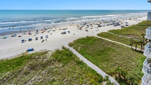 A beach with umbrellas, lounge chairs, and a pathway leading to a building.