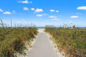 A beach pathway leading to the sea with a lifeguard tower and beach umbrellas in the background. - Awesome Atlantic views from this beautiful family condo w/pool, hot tub - steps from the sand (North Myrtle Beach)