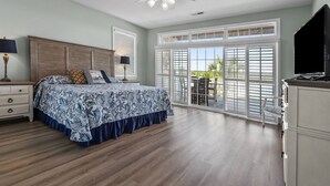 A bedroom with a large bed, a ceiling fan, a TV, and a view of the outdoors through a sliding glass door. - Elegant luxury channel home w/plenty of relaxing space inside & out-deck, floating dock, grill (North Myrtle Beach)