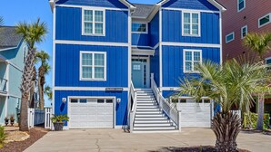 A two-story house with a blue exterior and white trim, featuring a front entrance with a set of stairs leading to the door. - Elegant luxury channel home w/plenty of relaxing space inside & out-deck, floating dock, grill (North Myrtle Beach)