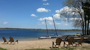 A beach with chairs and a sailboat. - Beach Harbor Resort - Beach House Cottage (Sturgeon Bay)