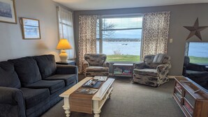 A living room with a large window, two armchairs, a sofa, a coffee table, and a TV. - Beach Harbor Resort - Beach House Cottage (Sturgeon Bay)