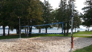 A beach volleyball court with a net, surrounded by sand and trees. - Beach Harbor Resort - Beach House Cottage (Sturgeon Bay)