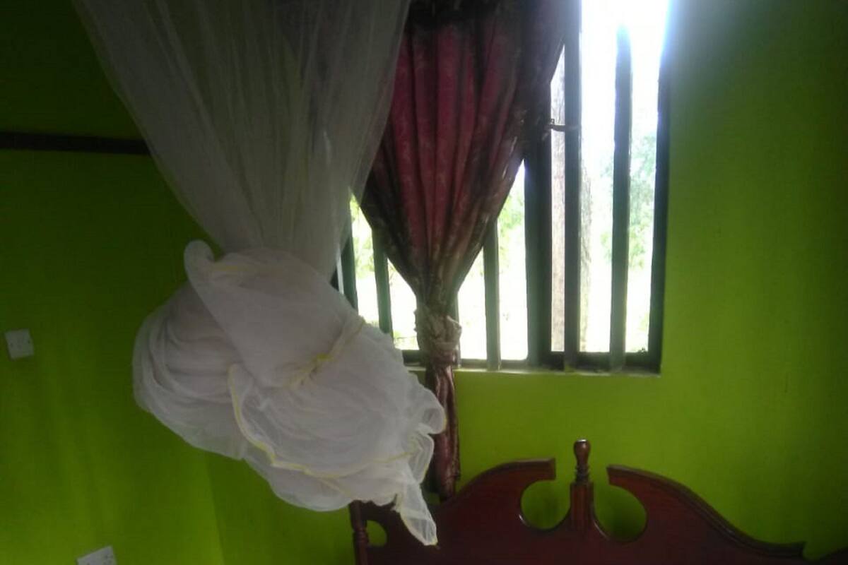 Um quarto com uma cama, uma janela com grades e uma cortina.