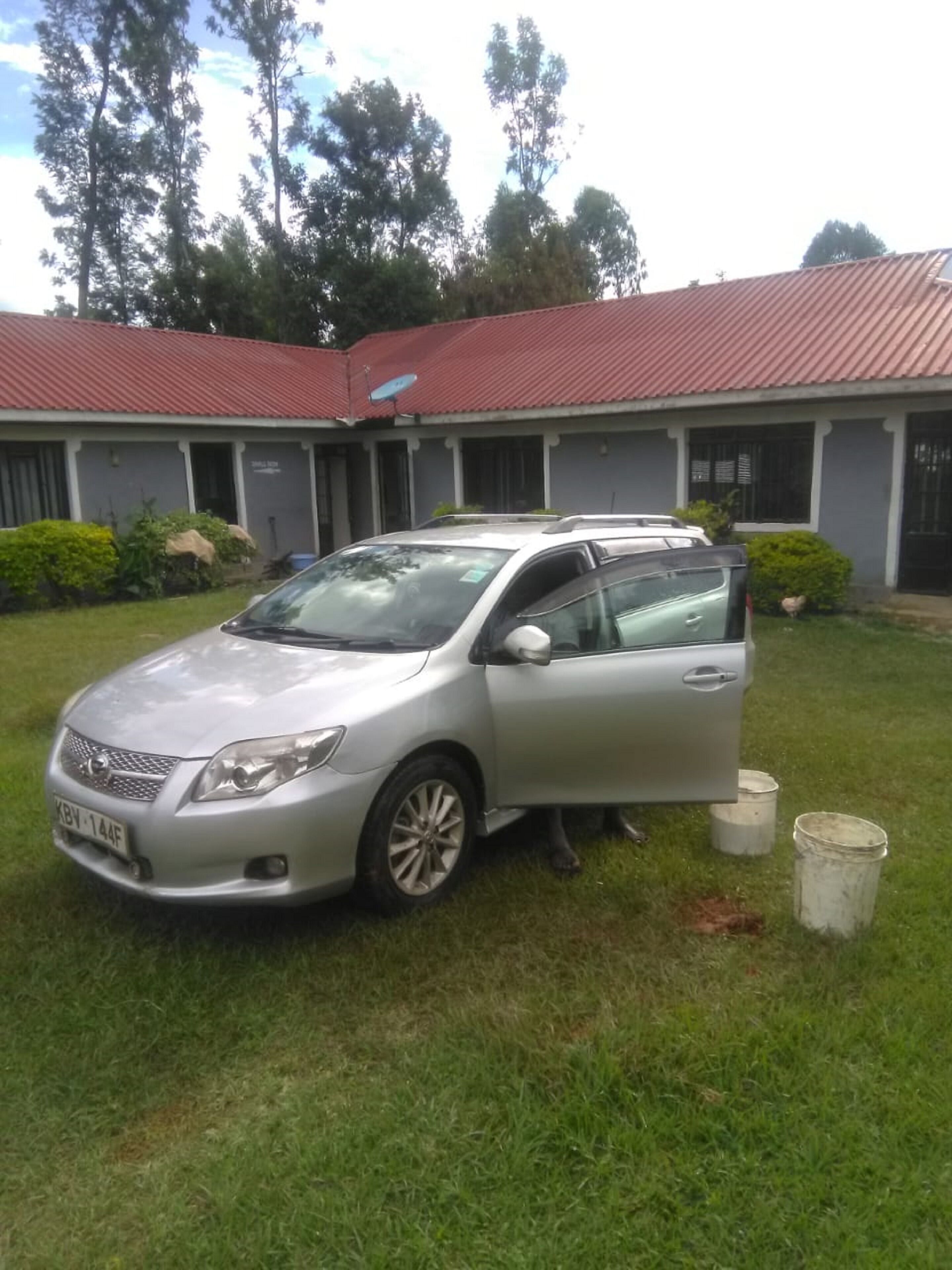 A silver car parked in front of a building with a red roof.