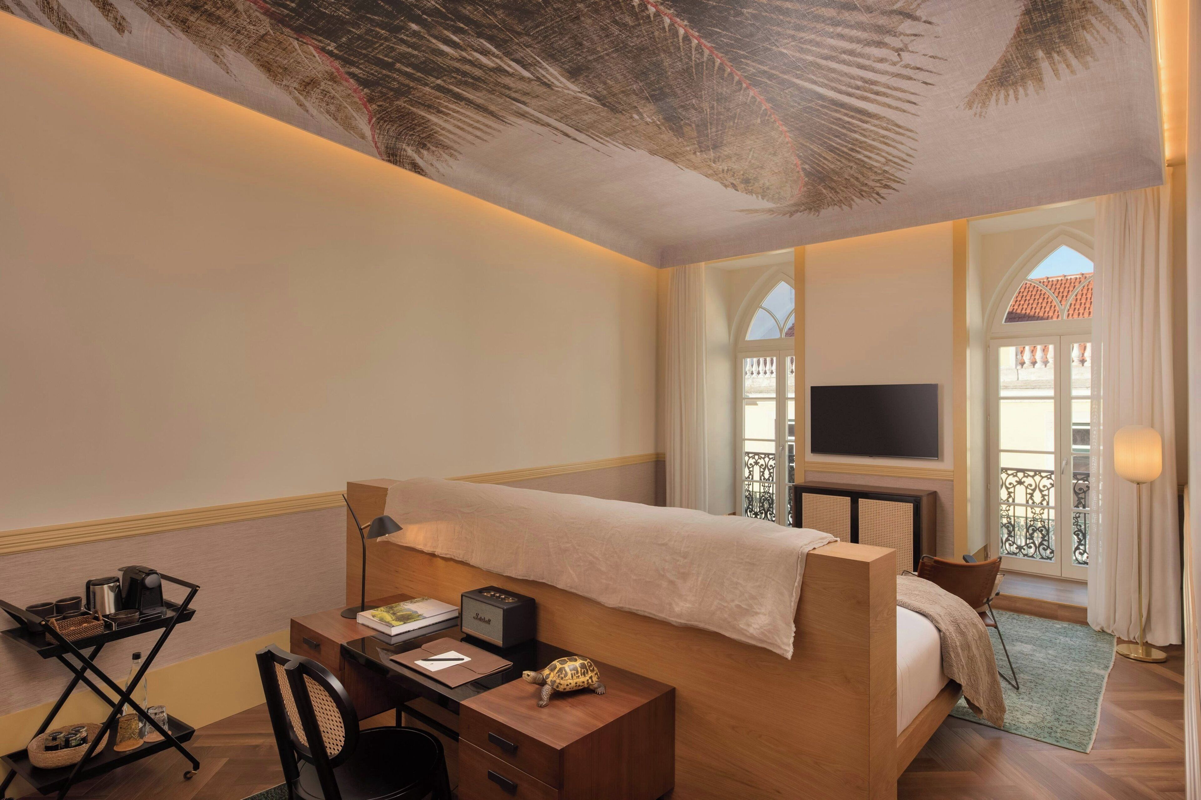 A hotel room with a bed, desk, chair, and a TV.