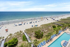 Un complexe hôtelier de bord de mer doté d’une piscine, de parasols et d’une tour de surveillance pour les sauveteurs.