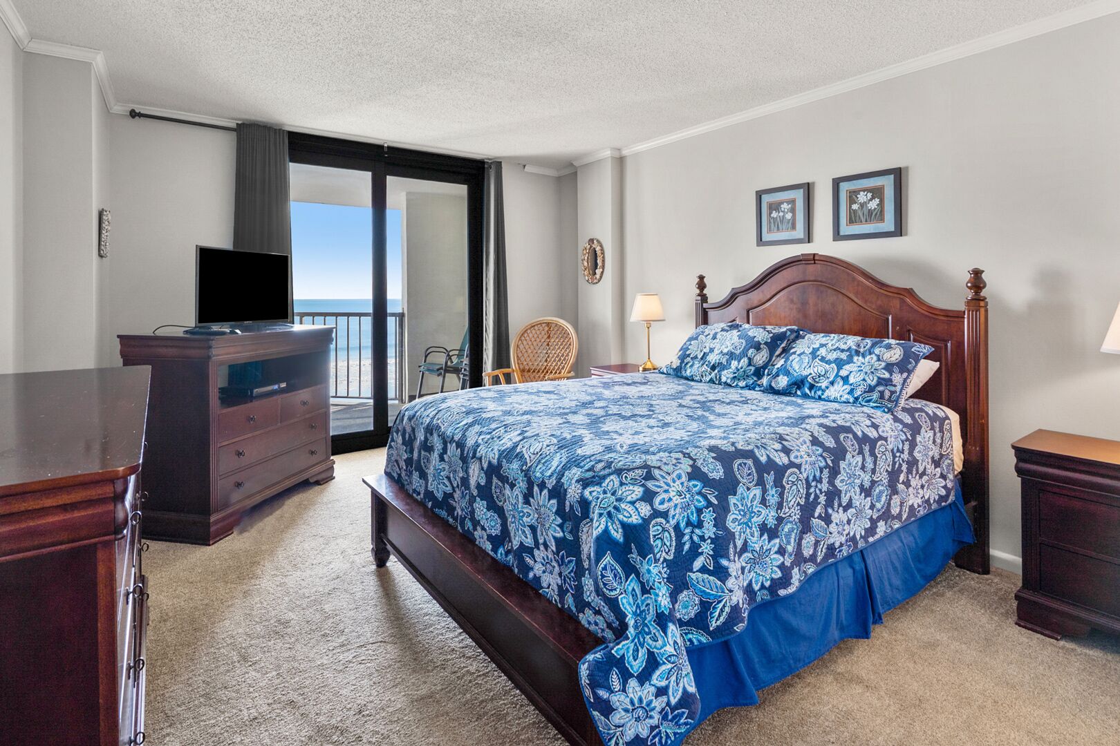 A bedroom with a large bed, a dresser, a TV, and a view of the ocean.