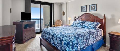 A bedroom with a large bed, a dresser, a TV, and a view of the ocean.