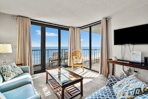 A room with a balcony, a sofa, a chair, a coffee table, and a TV. - Family friendly oceanfront resort in quiet Crescent Beach. Enjoy: condo, pool, grill, & sundeck (North Myrtle Beach)