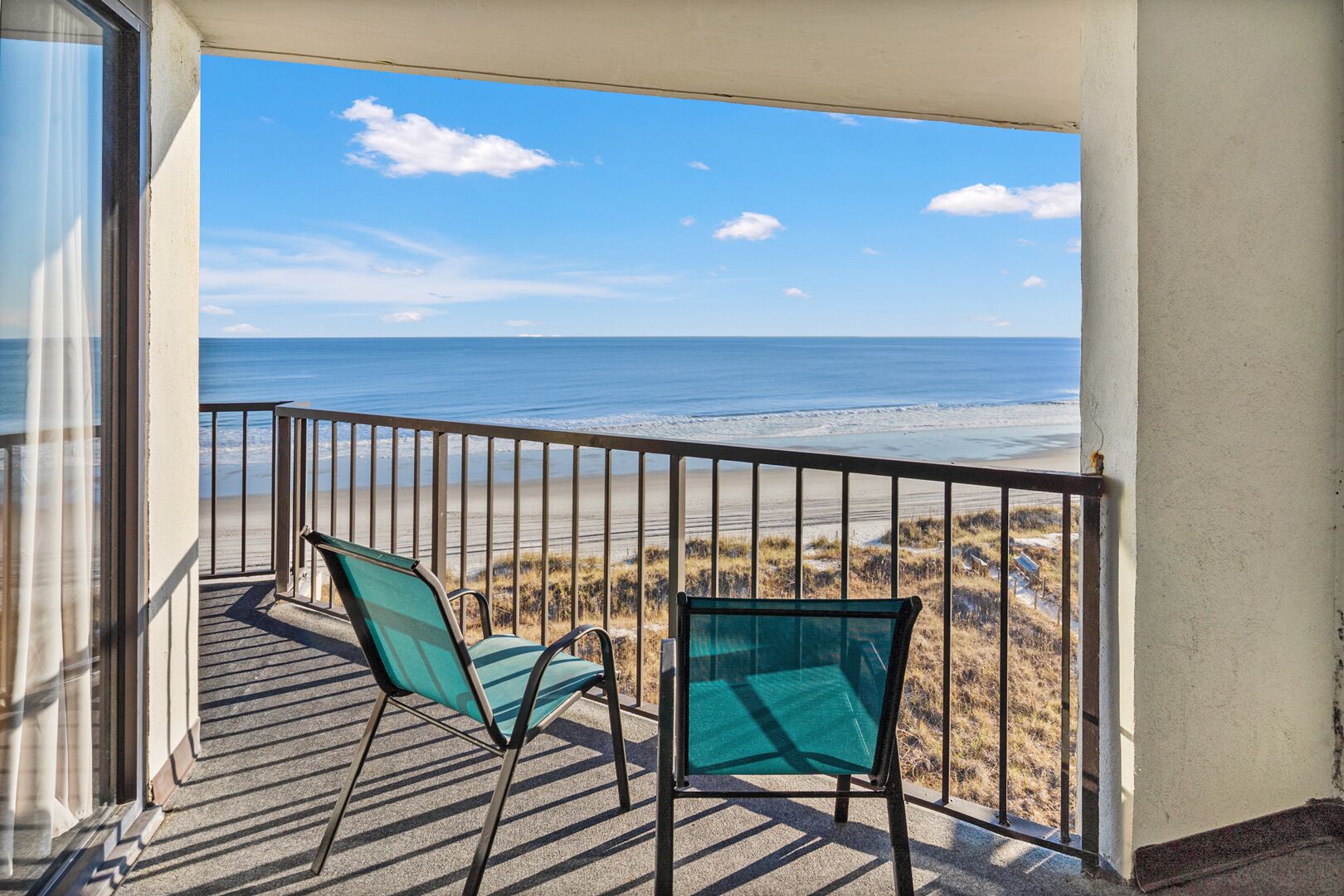 Een balkon met twee stoelen met uitzicht op een strand.