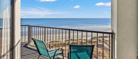 Een balkon met twee stoelen met uitzicht op een strand.