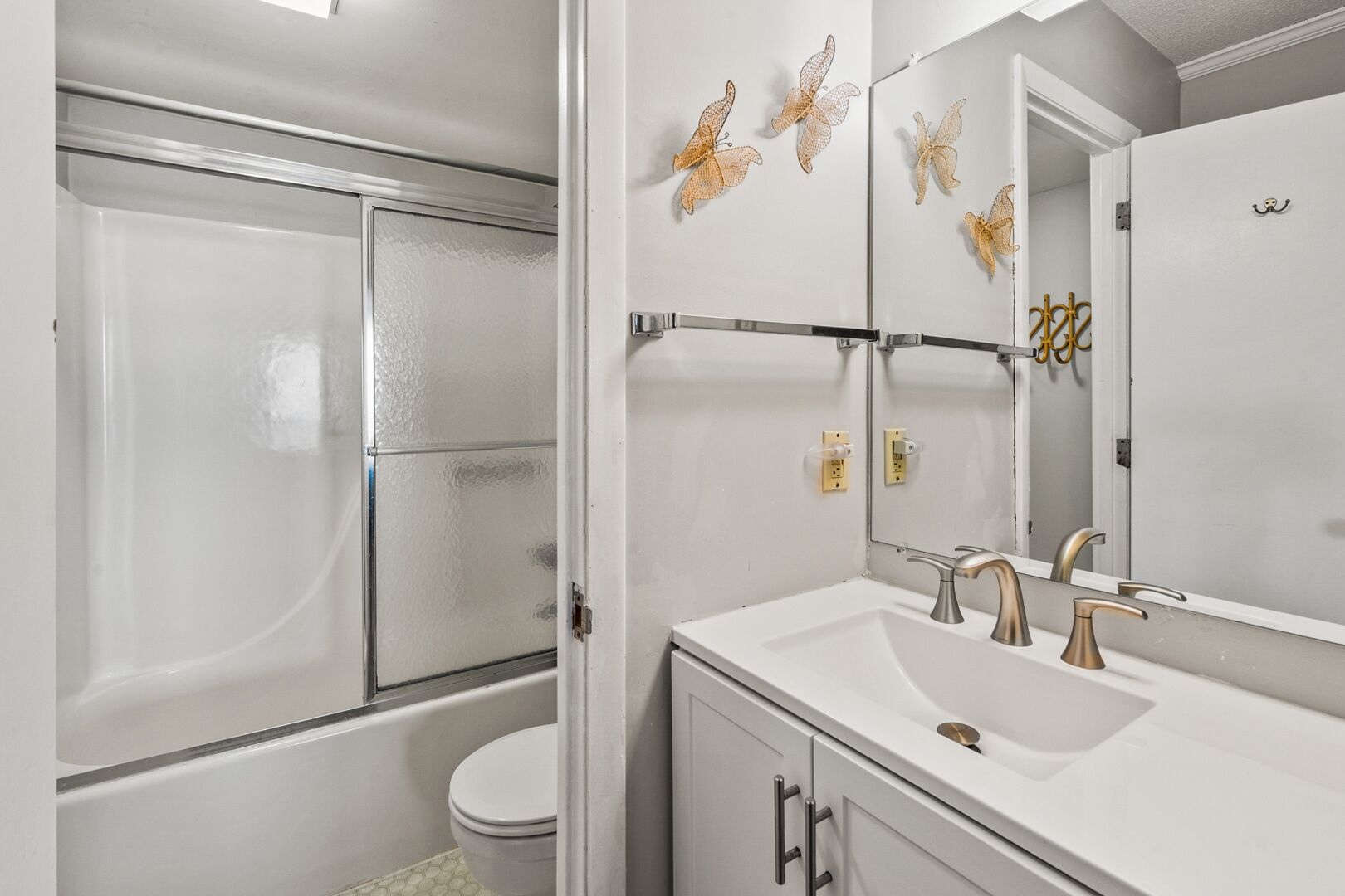 Ein Badezimmer mit Duschkabine, einem weißen Waschbecken mit goldfarbenen Armaturen und Wandbildern von Schmetterlingen.