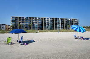 A beachfront hotel with multiple balconies, beach chairs, and umbrellas.