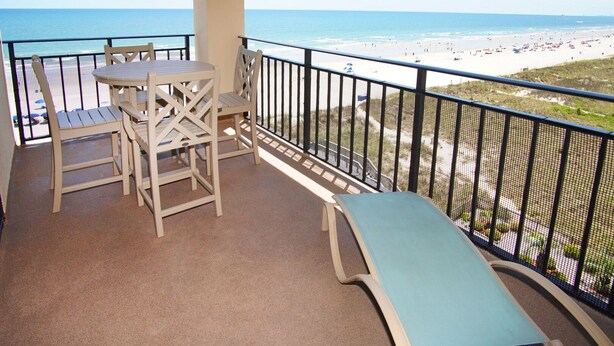A balcony with a table and chairs, a bench, and a view of the beach.