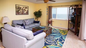 A living room with a sofa, coffee table, and a view of the ocean through a window.