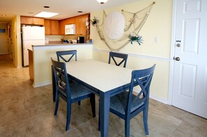 Un comedor con mesa y sillas, una cocina al fondo y una puerta a la derecha.