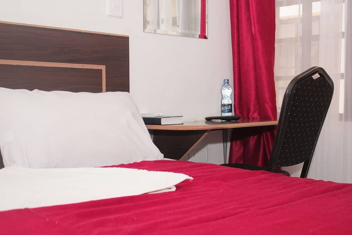 Habitación de hotel con cama, escritorio, silla, botella de agua y ventana con cortinas.