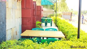 An outdoor seating area with green plastic chairs and a wooden table, surrounded by lush greenery. - Dover Hotel Bondo (Bondo)