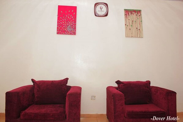Una habitación con dos sillones tapizados en terciopelo rojo, un cuadro abstracto rojo, un reloj y un adorno en la pared.