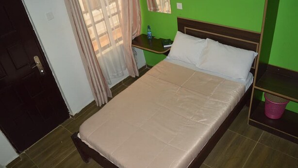 A single bed with a beige mattress and white pillows in a room with green walls and a wooden floor. - Dover Hotel Bondo (Bondo)