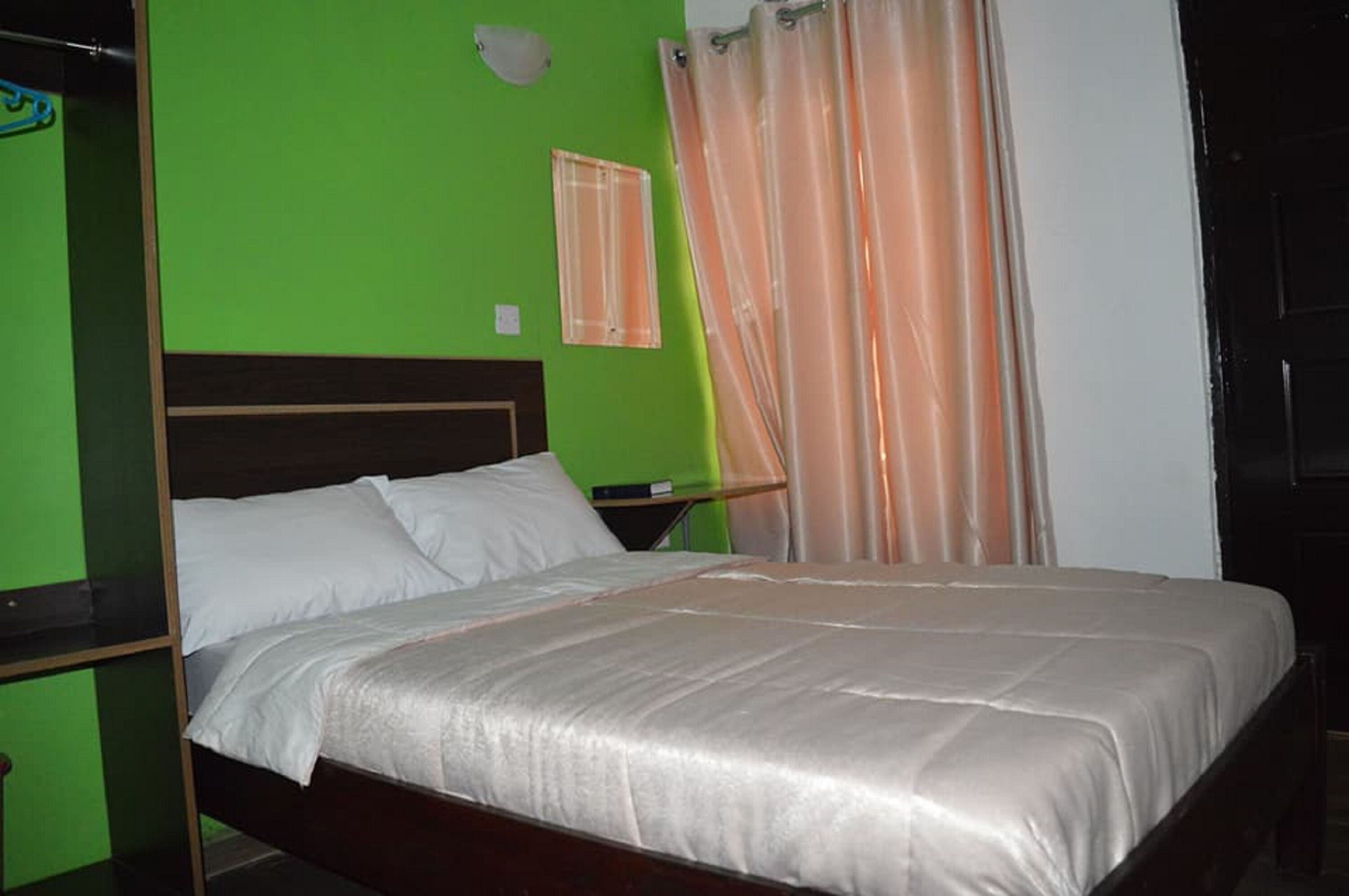 A bed with a white mattress and a beige blanket in a room with green walls and a wooden headboard.