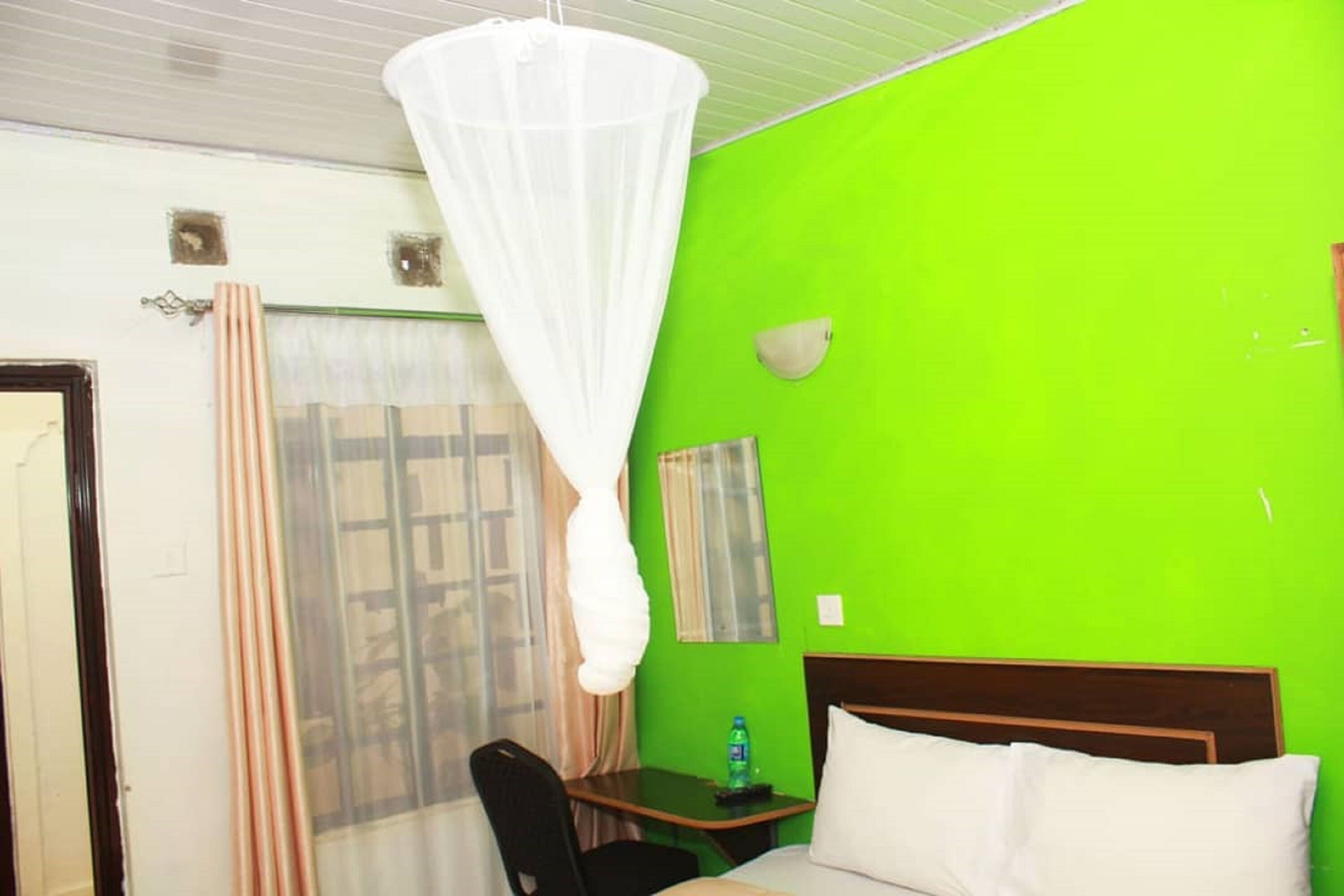 A room with a bed, a desk, a chair, a mosquito net, and a window with curtains.