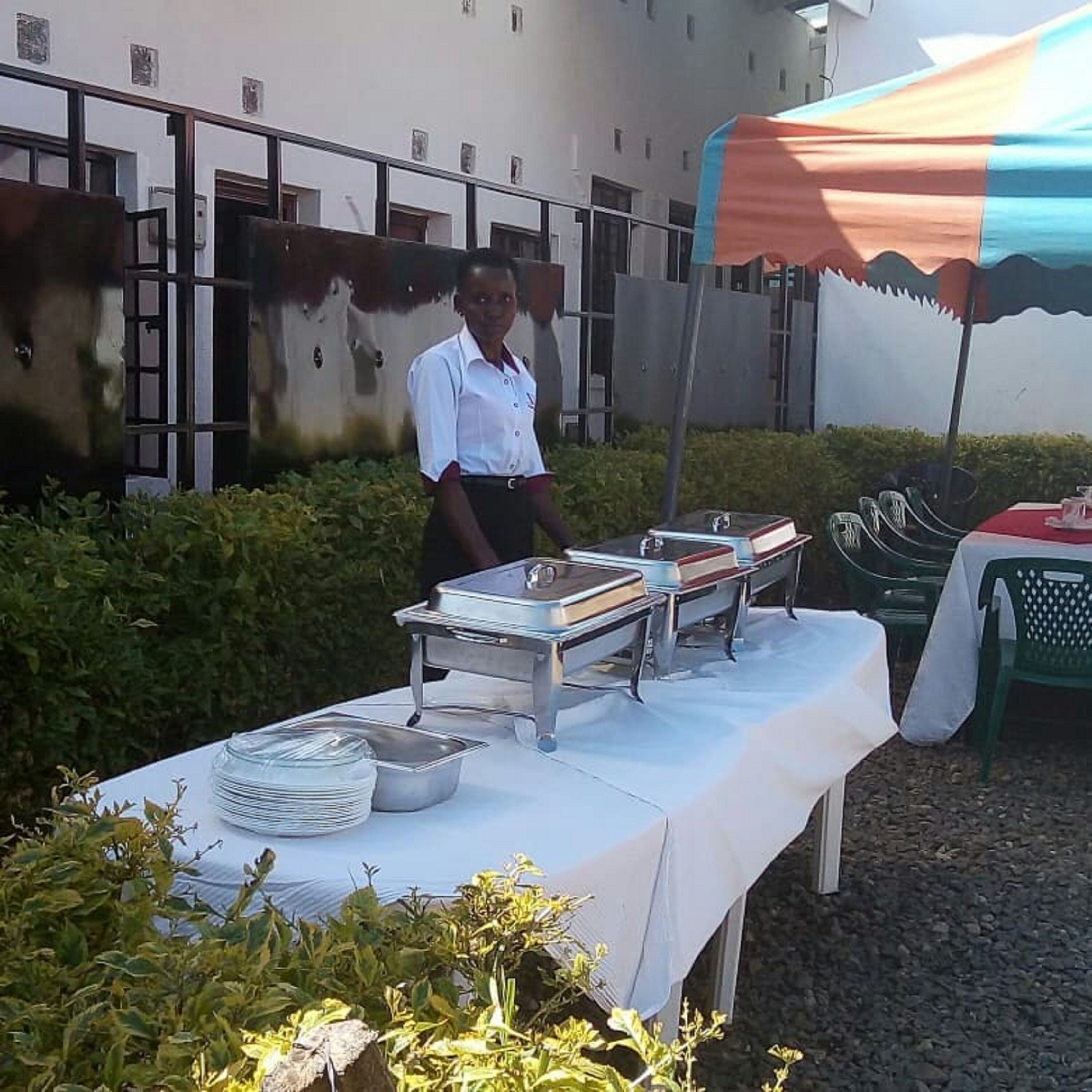 A buffet table with various dishes and serving utensils, set up outdoors with a building in the background.