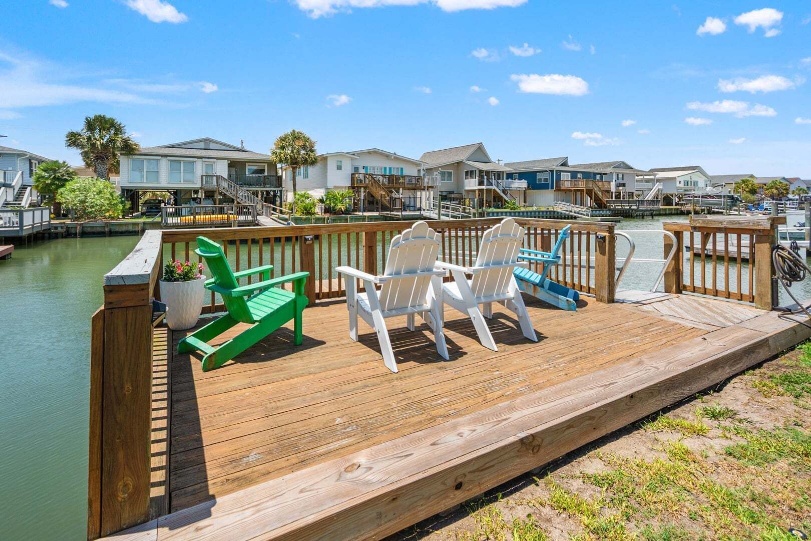 A wooden deck with Adirondack chairs overlooking a marina with boats and houses.