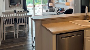 A modern kitchen with a built-in dishwasher, a dining area with white chairs, a large TV mounted on the wall, and a view of a dock and boats through the windows. - 4BR/3BA Lakefront Penthouse, Clearwater Condominiums<br>Sleeps 8 (Camdenton)