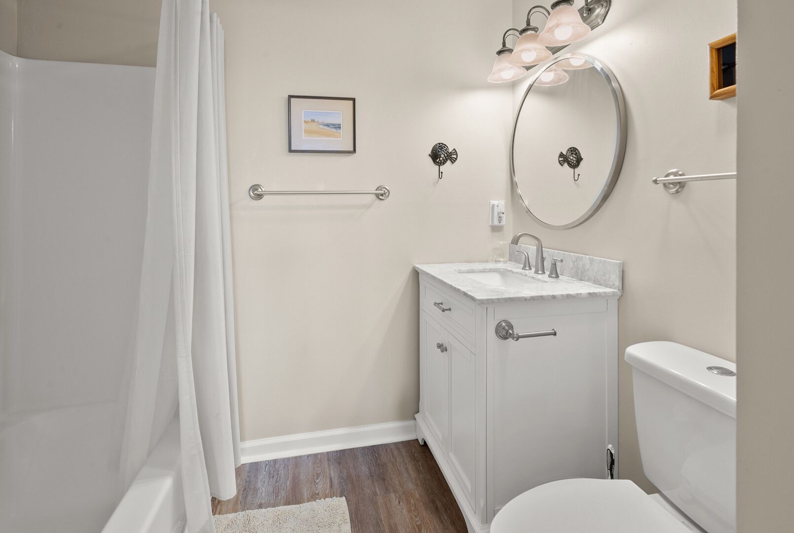 A bathroom with a shower, toilet, sink, and a mirror with lights.