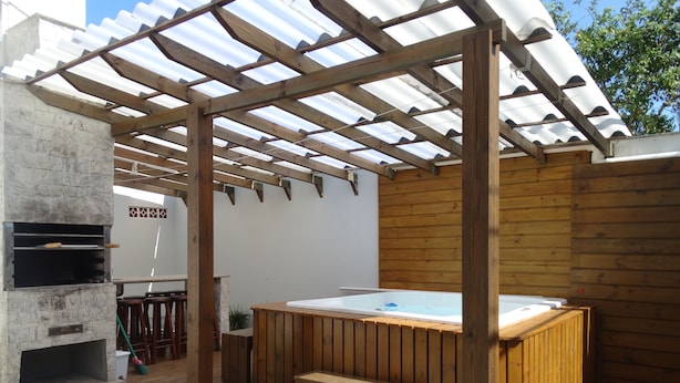 Een houten terras met een jacuzzi, een barbecue en een stenen open haard.