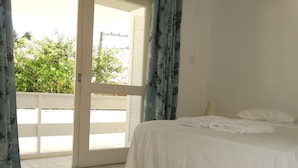 Een slaapkamer met een bed, witte gordijnen en uitzicht op groen.