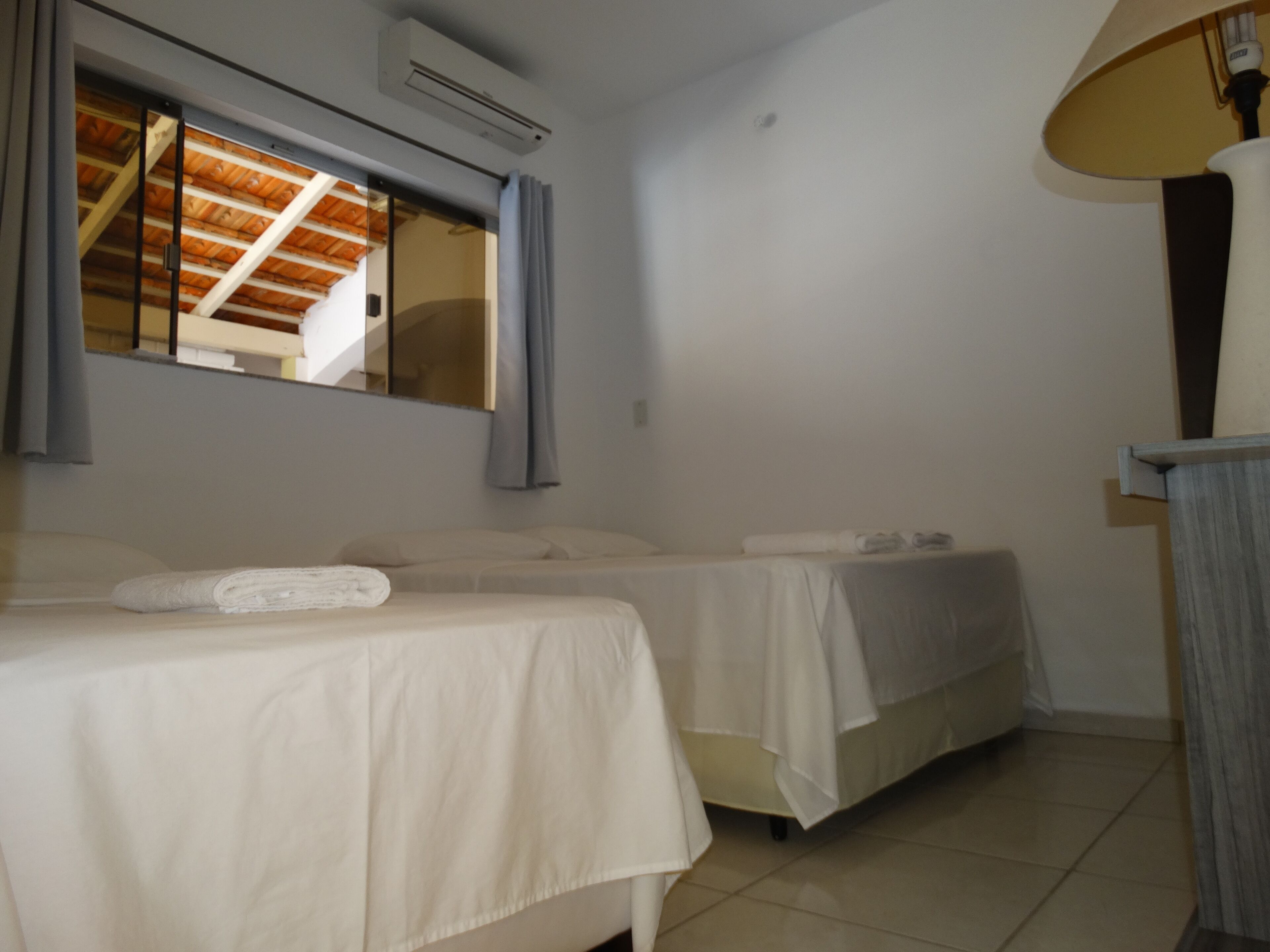 Ein Hotelzimmer mit zwei Betten, einem Fenster mit Vorhängen, einer Klimaanlage und einer Lampe.