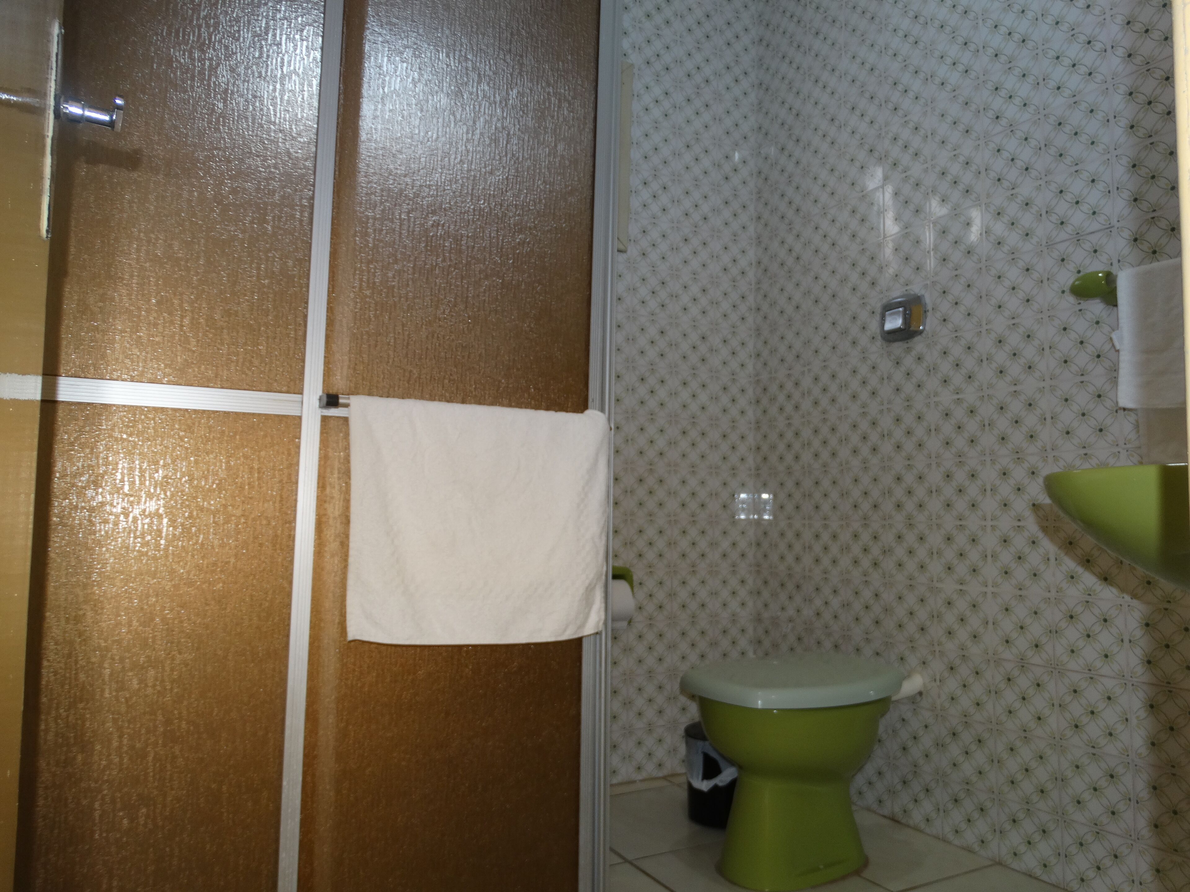Une salle de bain avec des toilettes vertes, un lavabo blanc et un mur de douche orné d’un motif.