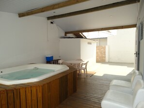 Een houten terras met een jacuzzi, buitenmeubels en uitzicht op de omgeving.