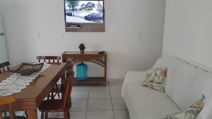 Zona pranzo con tavolo in legno, sedie e distributore d'acqua blu. Un televisore è montato sulla parete sopra il tavolo.