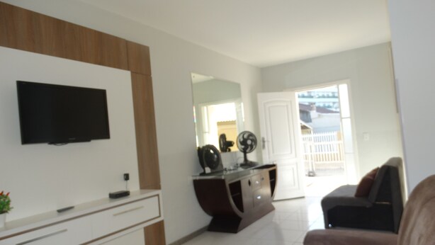 Uma sala de estar moderna com televisão de tela plana na parede, um sofá, uma mesa de centro e uma pequena mesa lateral com uma planta.