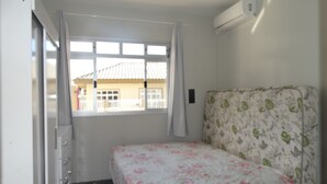 Quarto com cama, janela, ar condicionado e porta.